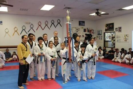 A group of students around another black belt student who has won a six foot trophy